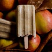 Beige popsicle with apple pieces in it and cinnamon flecks sitting on top of apples.