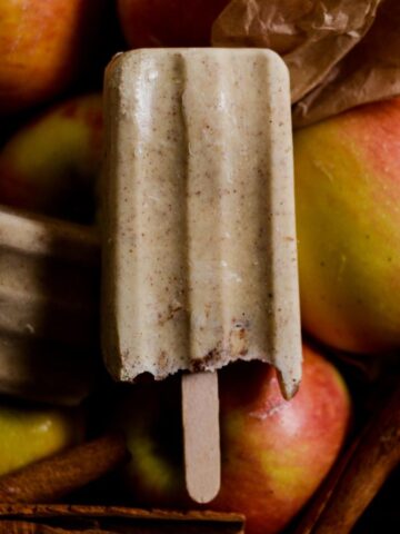 Beige popsicle with apple pieces in it and cinnamon flecks sitting on top of apples.