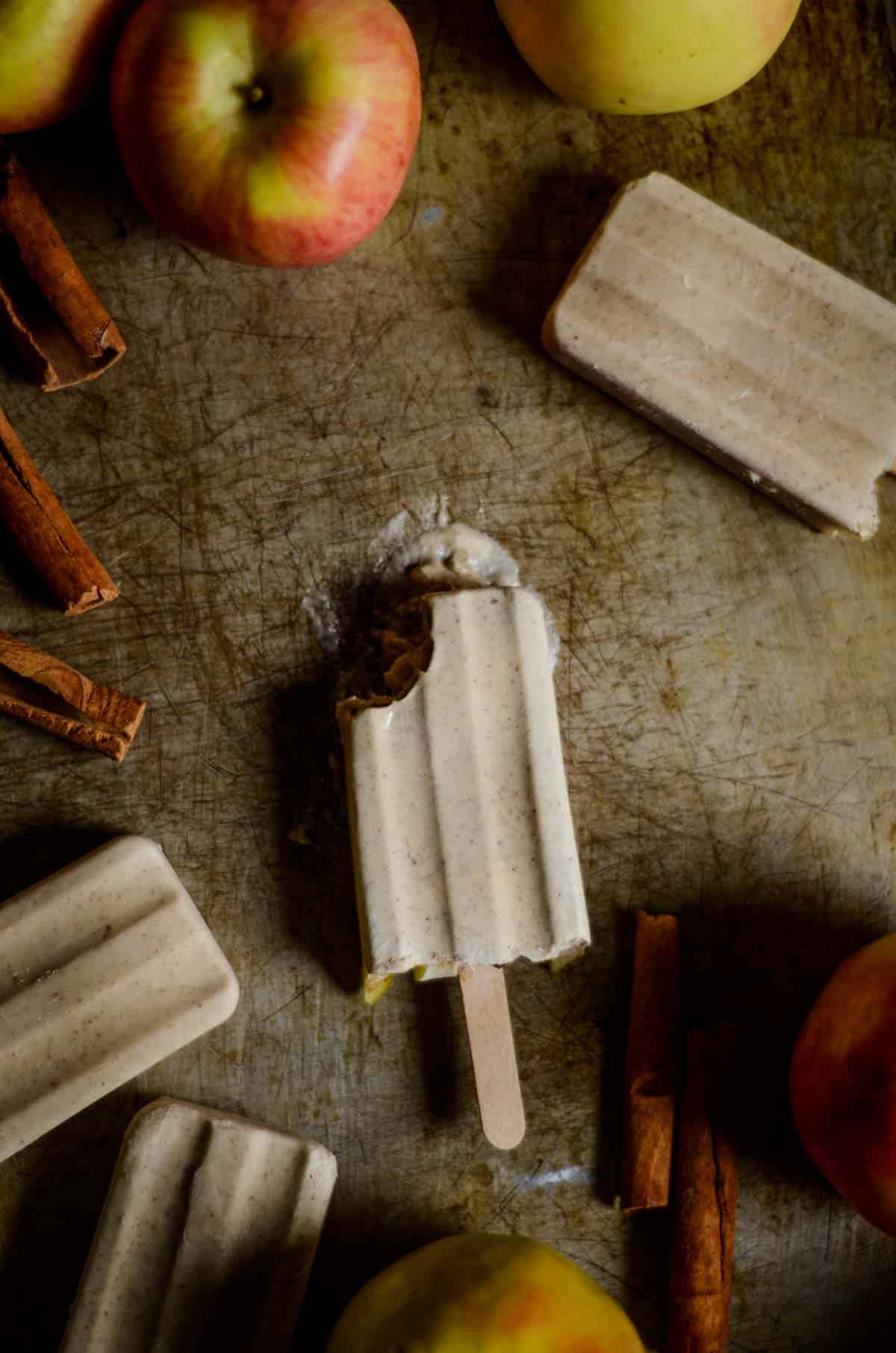 Beige popsicle with bite missing from it on the counter with apples.