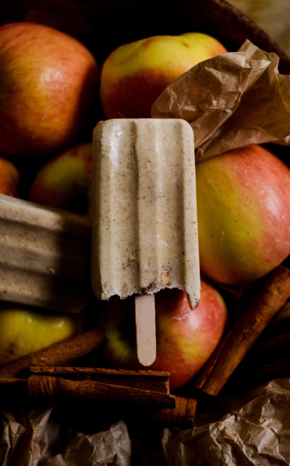 Apple popsicle in a bowl of yellow and red apples and cinnamon.