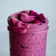 pink dragon fruit banana smoothie in a glass cup with fresh pink dragon fruit on top.