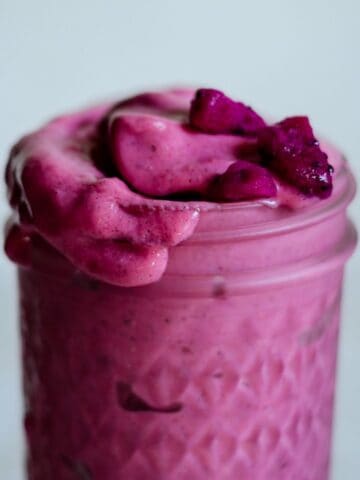 pink dragon fruit banana smoothie in a glass cup with fresh pink dragon fruit on top.