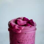 Bright pink smoothie in a glass jar spilling over the side.