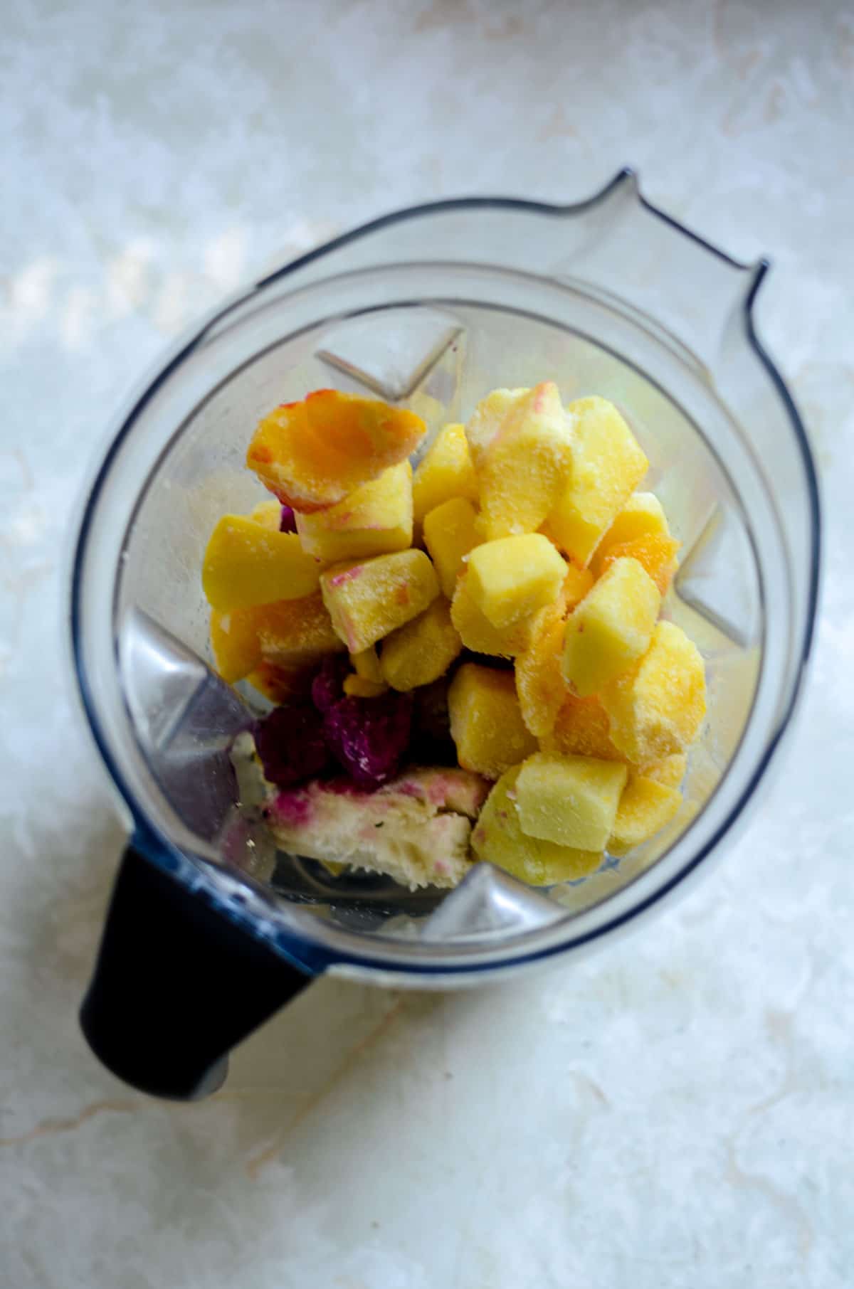 Banana, dragon fruit, pineapple, and hemp hearts in the blender for a smoothie.