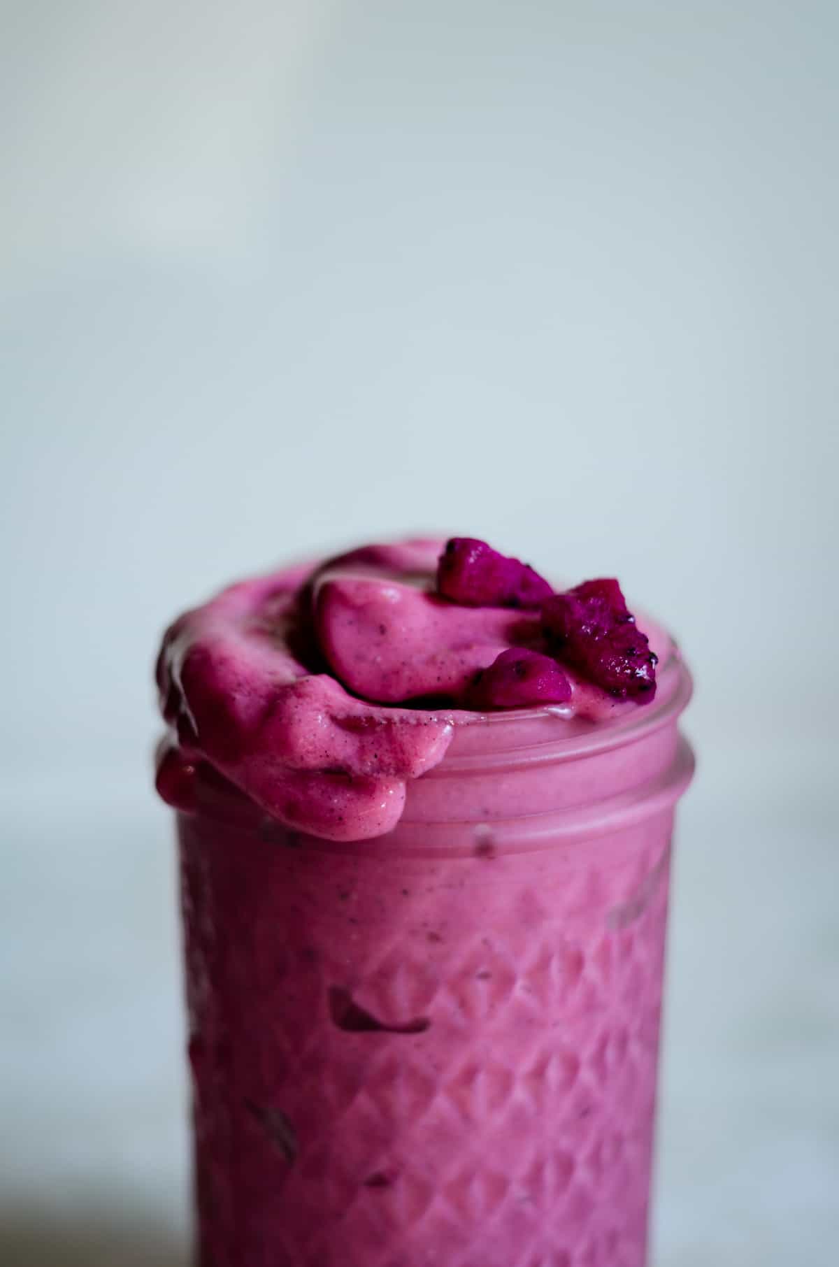 Bright pink dragon fruit smoothie in a glass jar with a couple chunks of purple pitaya on top.