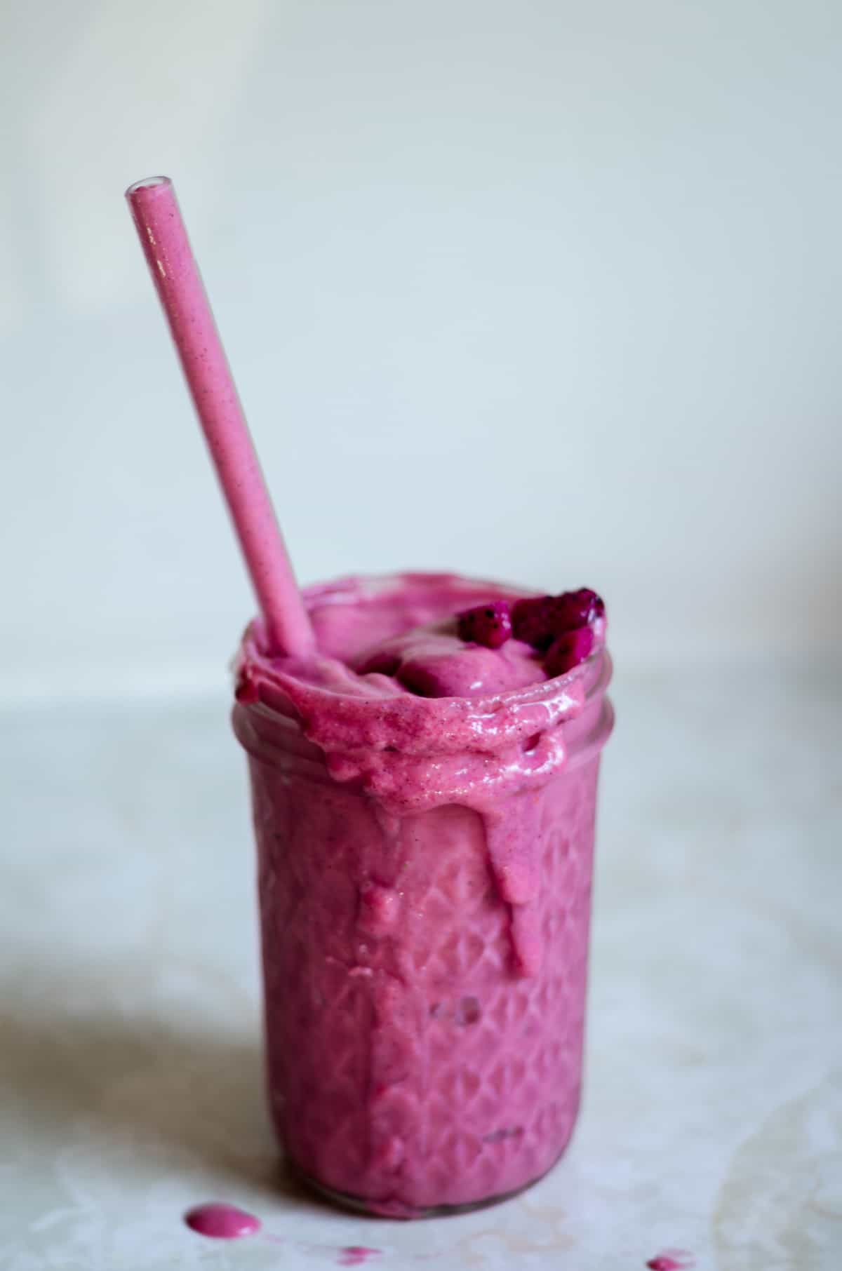 Pink dragon fruit smoothie with banana in a glass jar with a clear straw.