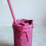 Pink smoothie spilling out of a jar with a straw.