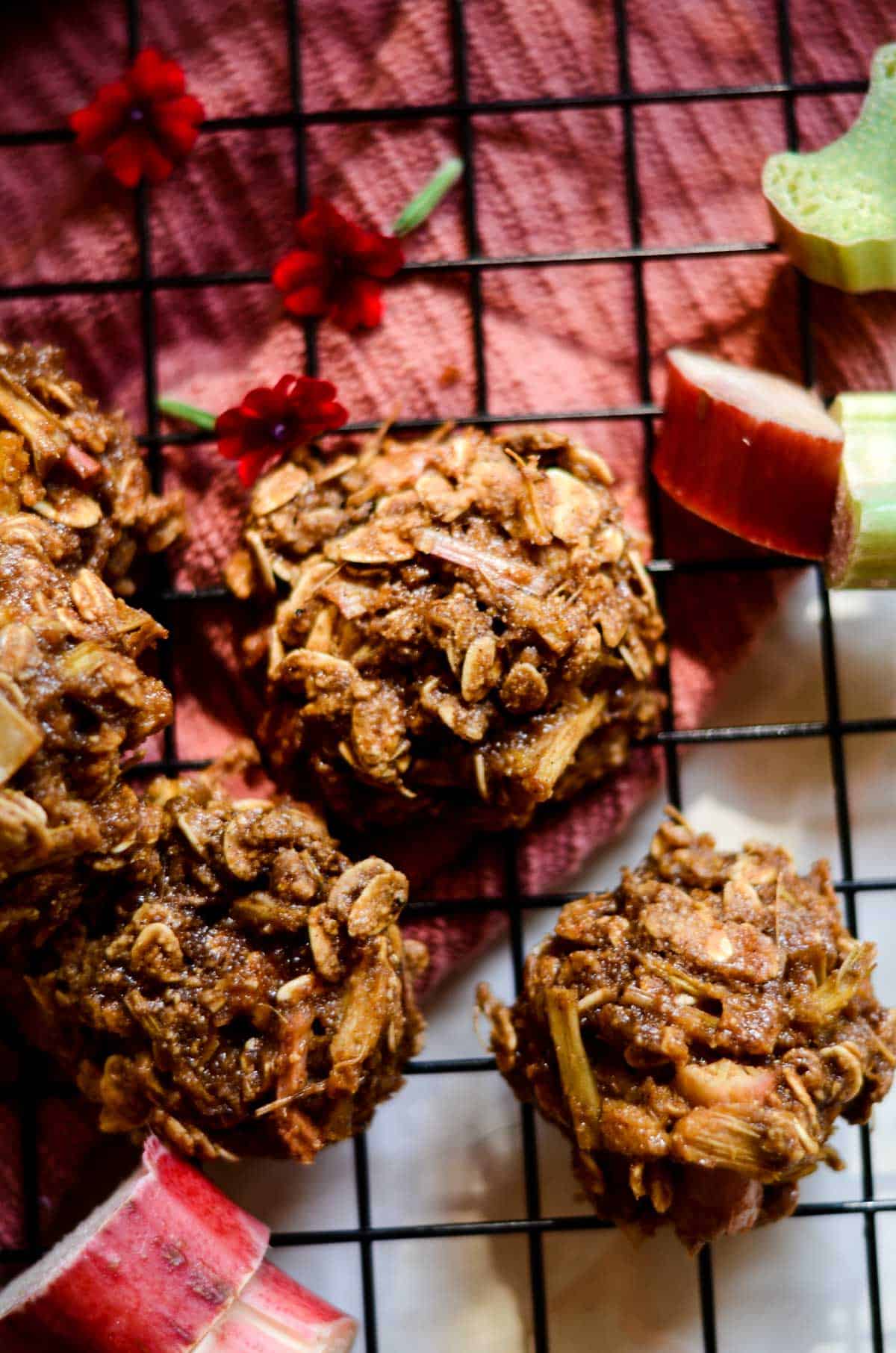 Brown rhubarb oatmeal cookies on a cooling rack with pieces of rhubarb and a pink towel.