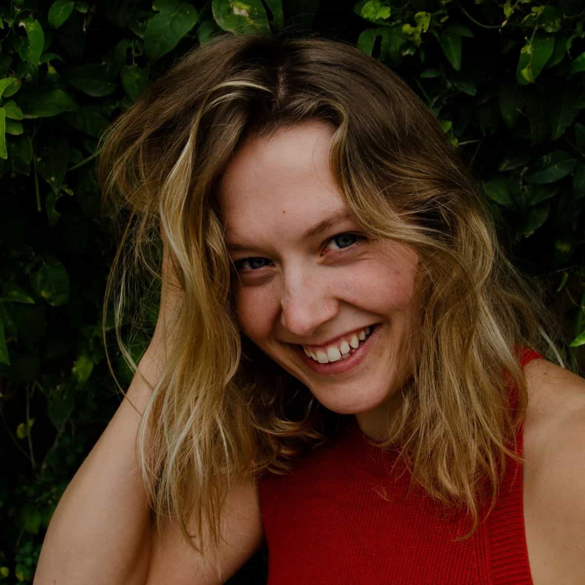 Girl with light skin smiling with her teeth showing with light brown hair to her shoulders.