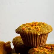 Orange colored muffin with zest flecks on top.
