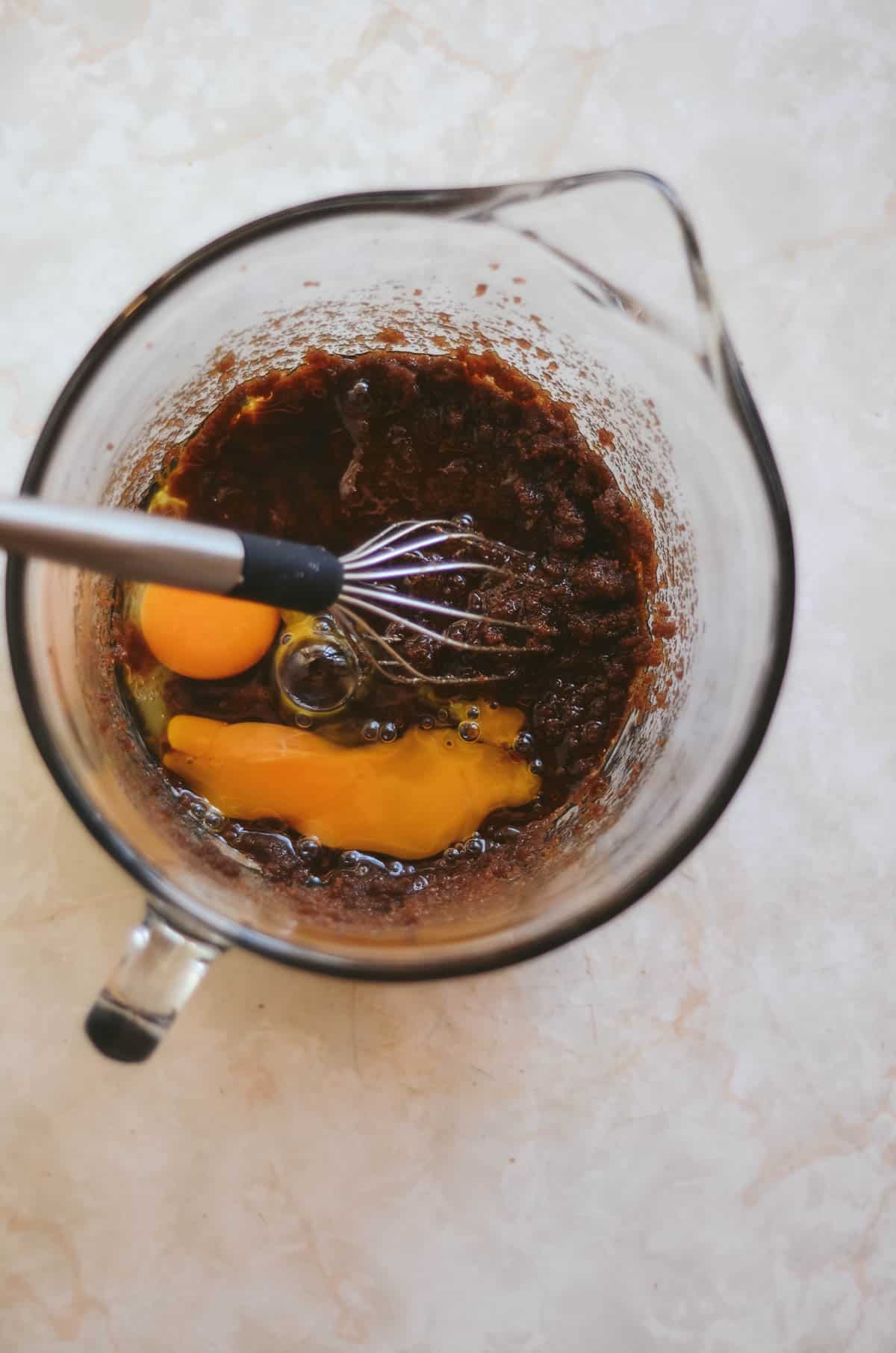 Raw eggs in glass bowl being whisked into coconut sugar.