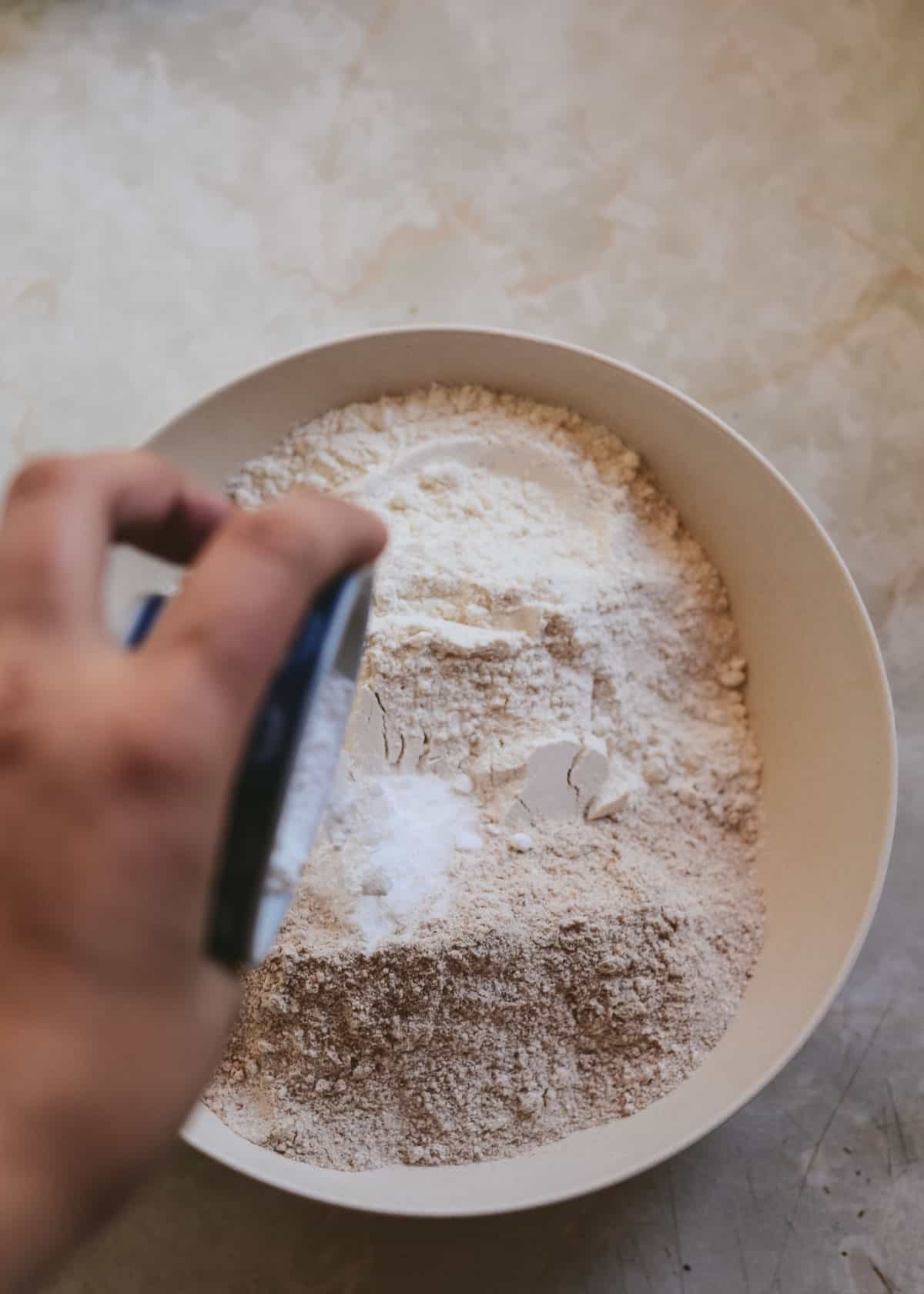 Whole wheat flour, white flour, baking powder, baking soda being mixed together.