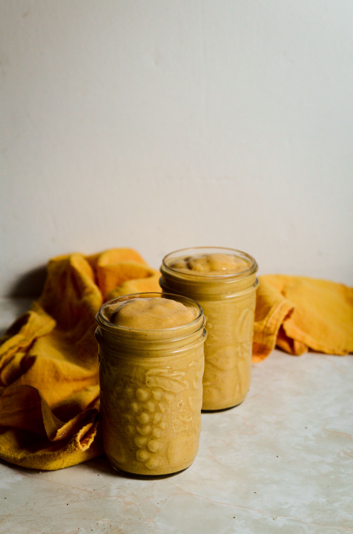 Two orange yellow smoothie in jars.