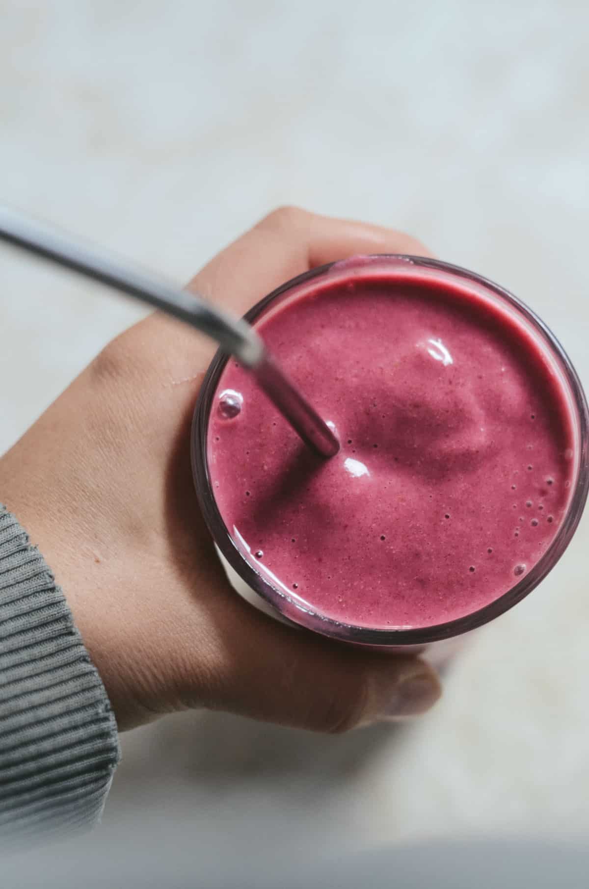 Hand holding cup with pink smoothie.