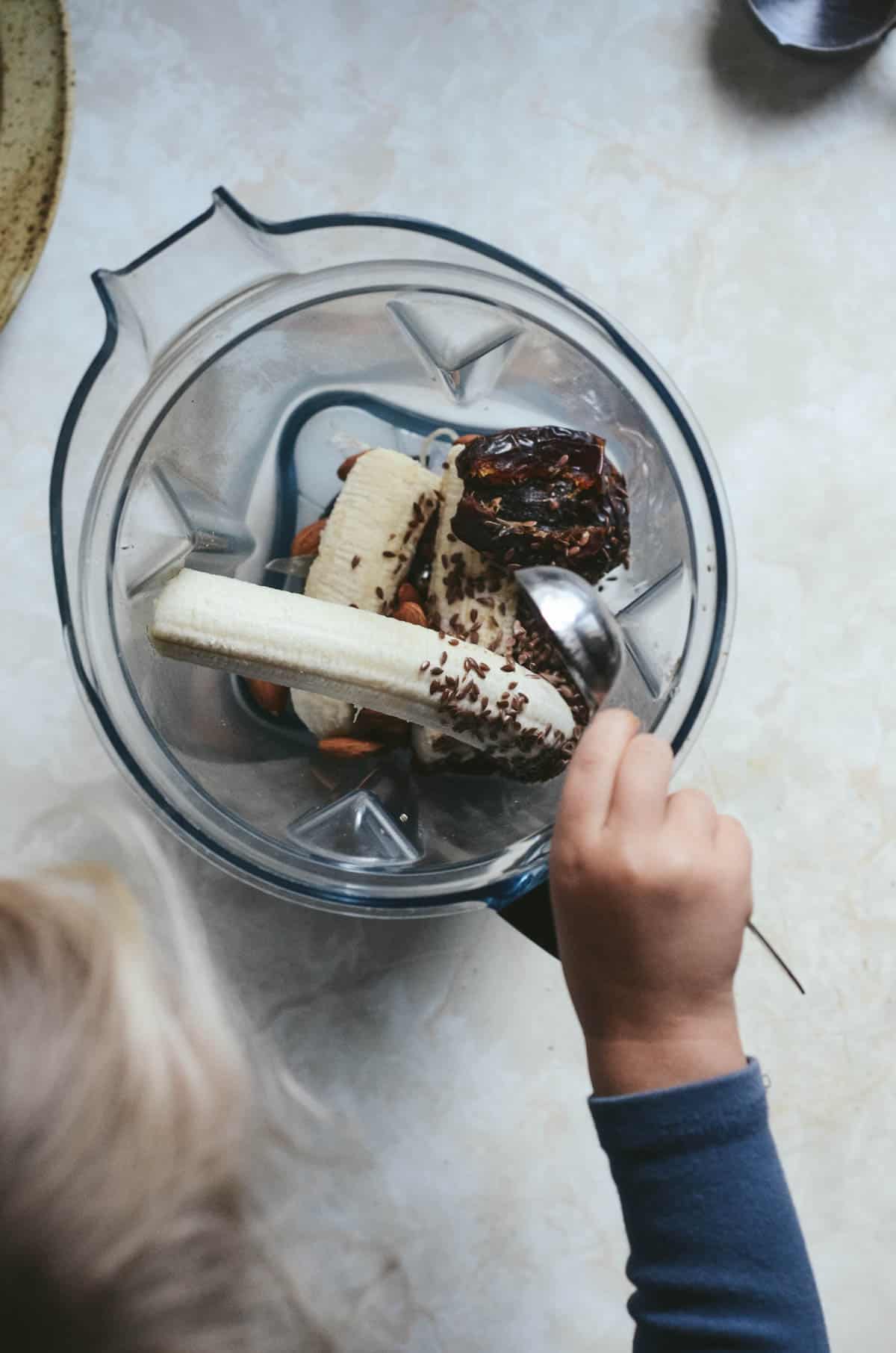 Toddler placing banana in blender.