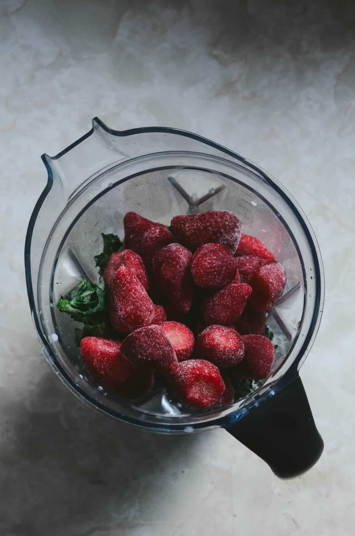 Frozen strawberries on top of kale in vitamix.
