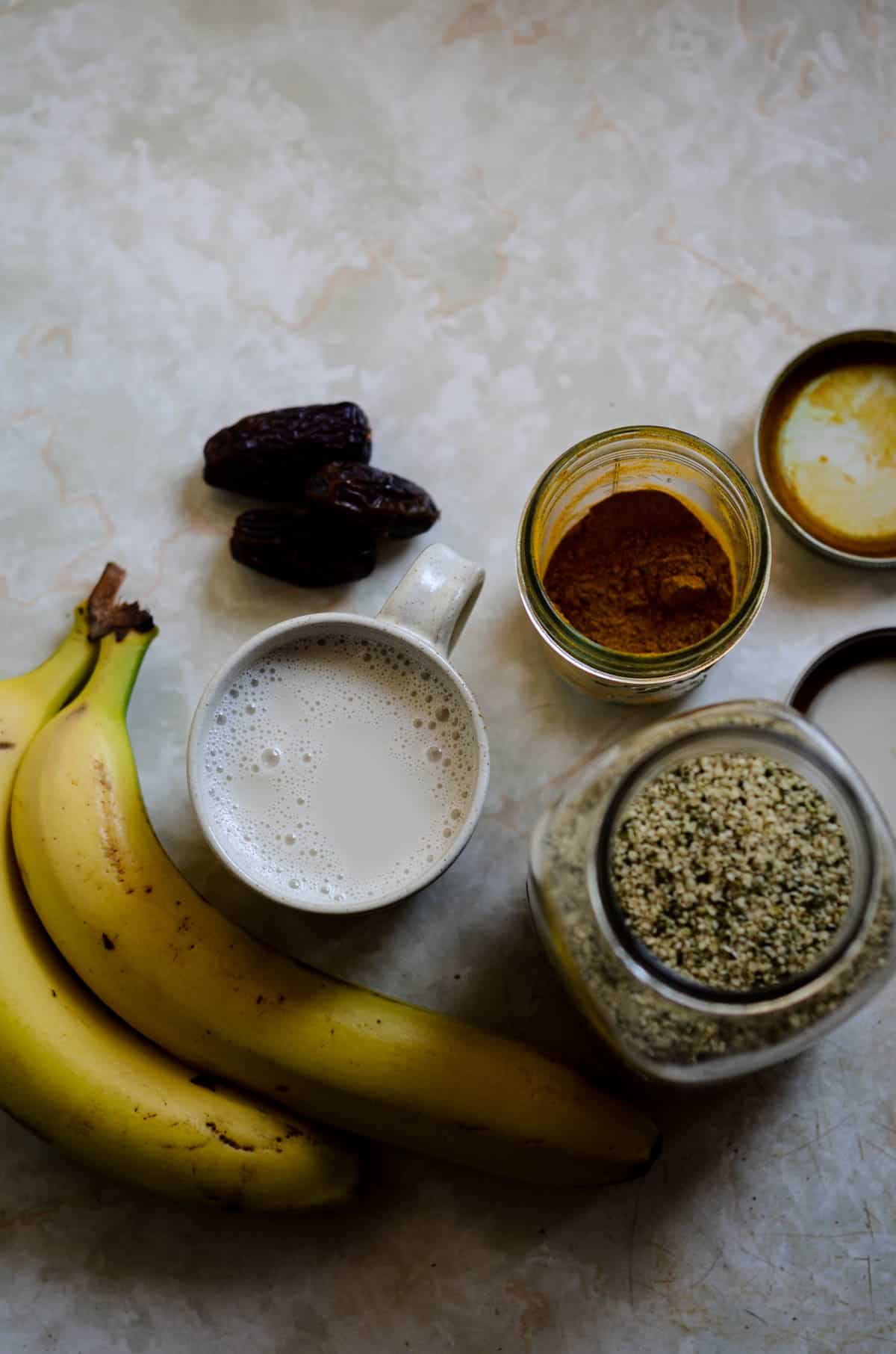 Bananas, milk, dates, golden milk mix, hemp hearts on a counter.