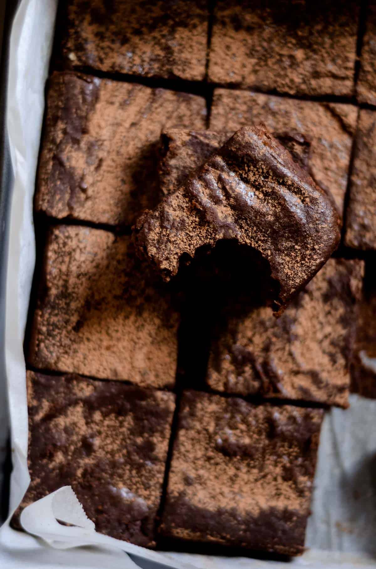 Brownie with bite missing sitting on top of a pan of cut fudgy brownies.