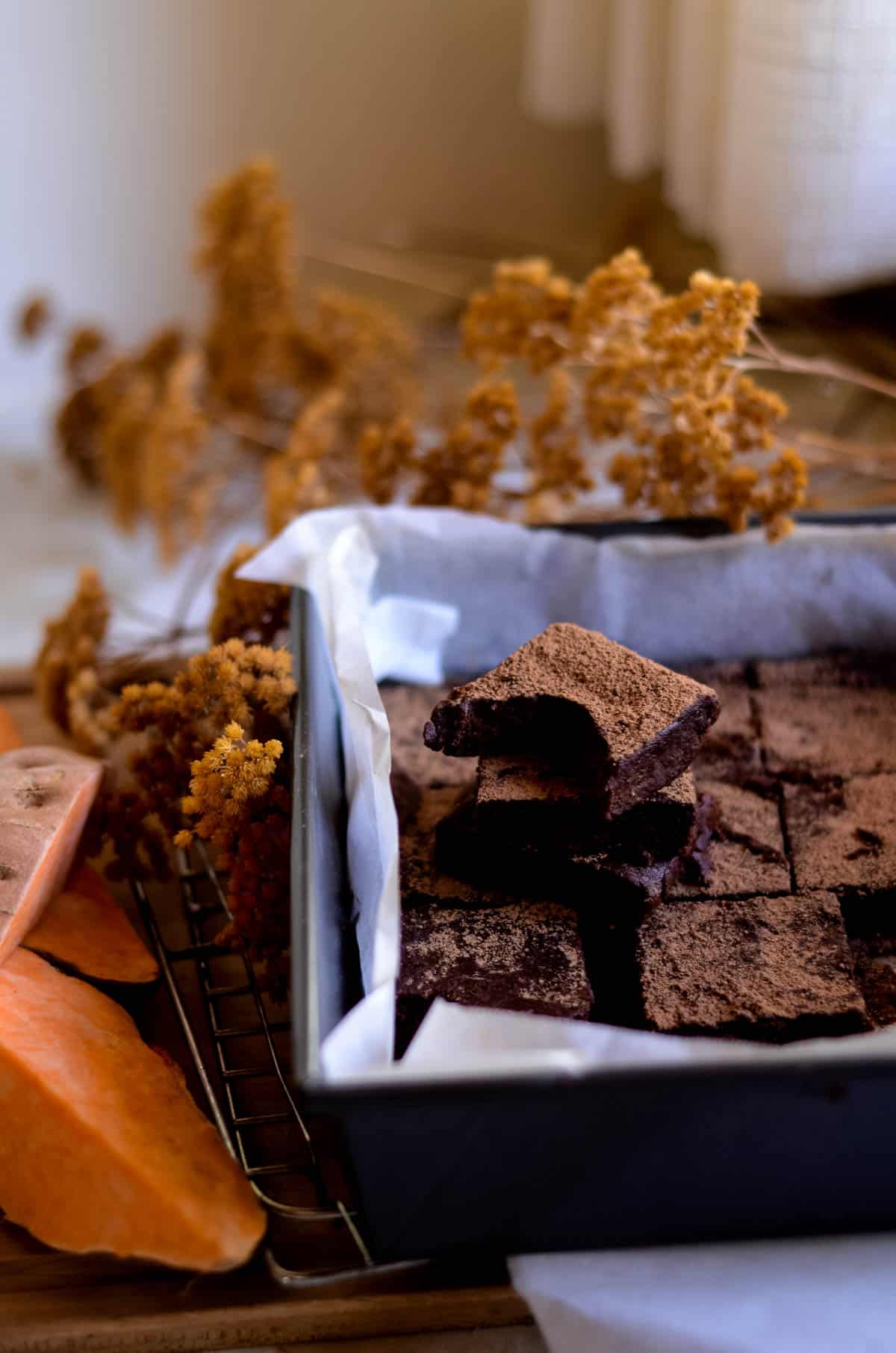 Fudgy chocolate brownie with bite missing in baking pan beside cut sweet potatoes.