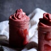 Two thick strawberry smoothies in small jars with strawberries on the side.