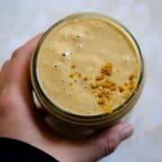 Yellow smoothie in jar with turmeric powder on top.