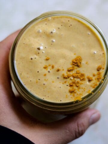 Yellow smoothie in jar with turmeric powder on top.