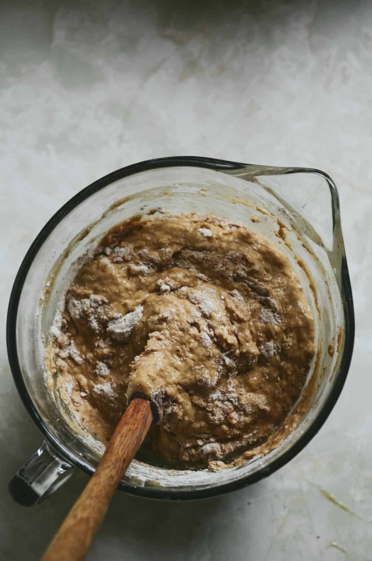 Spatula stirring the muffin batter in a glass bowl. 