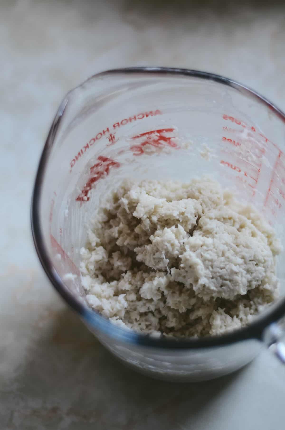 Mixing coconut milk and desiccated coconut in a glass measuring cup.