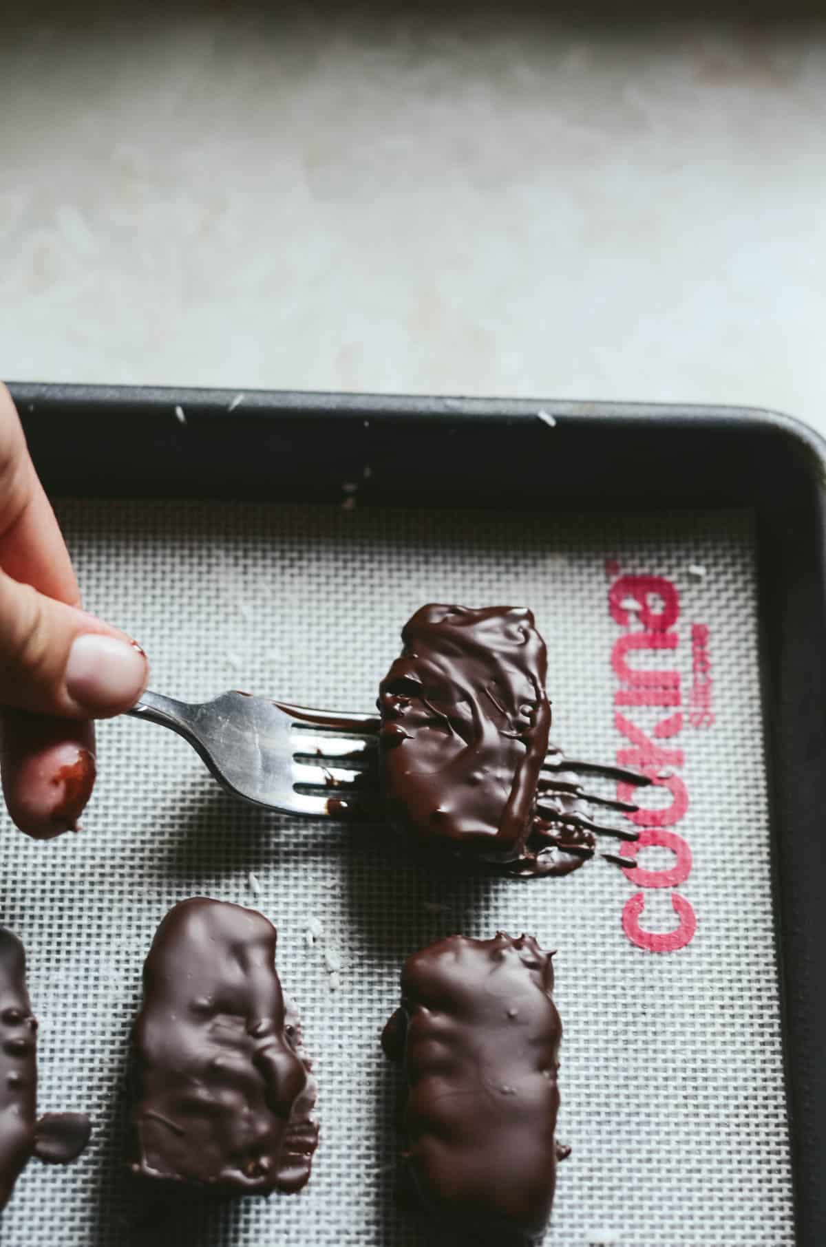 Coconut log covered in melted chocolate being placed on a cookie sheet.