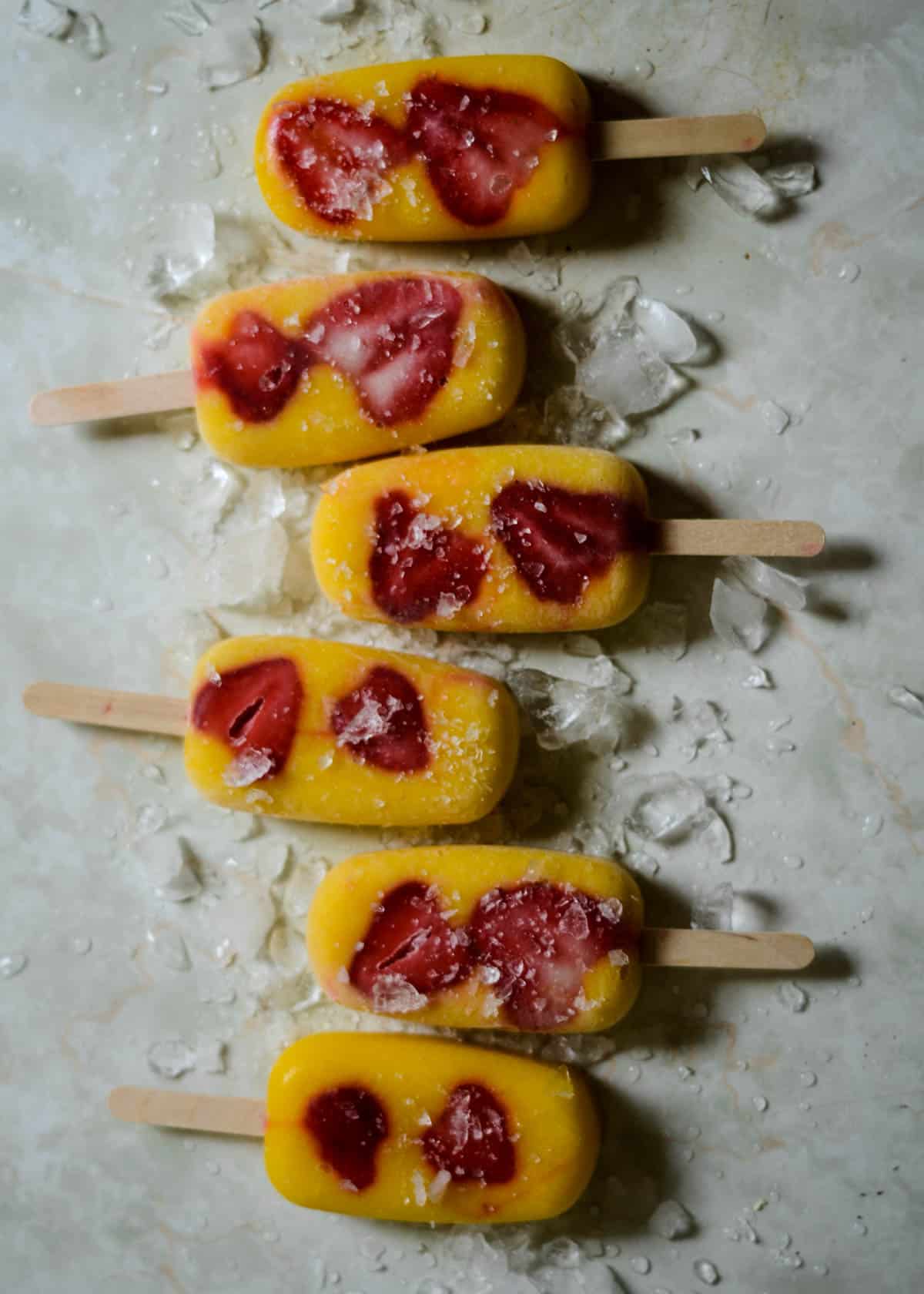 Six mango strawberry, bright yellow and red popsicles with ice.