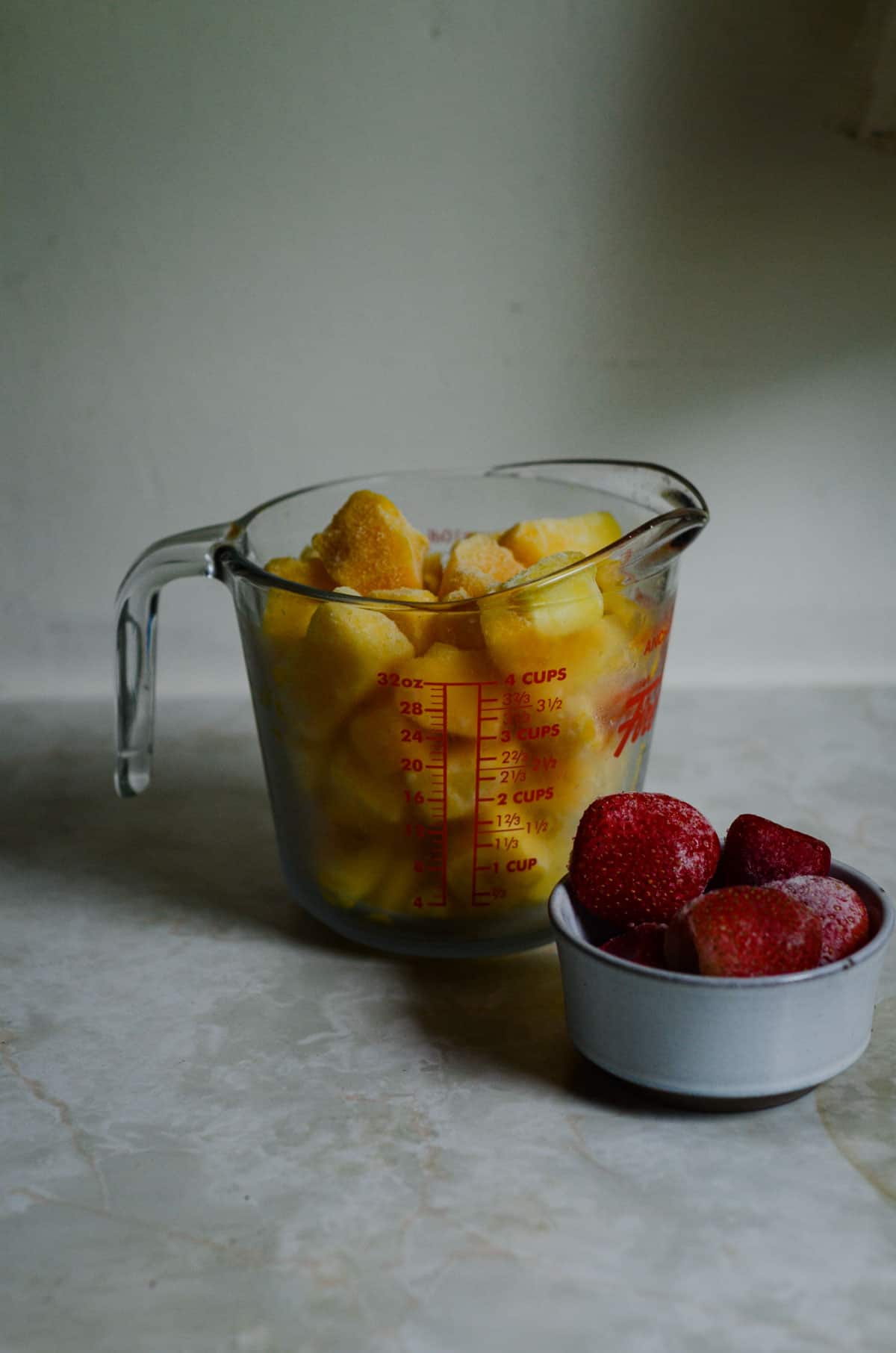 Two ingredients, frozen mango and strawberries measured on the table for mango popsicles.