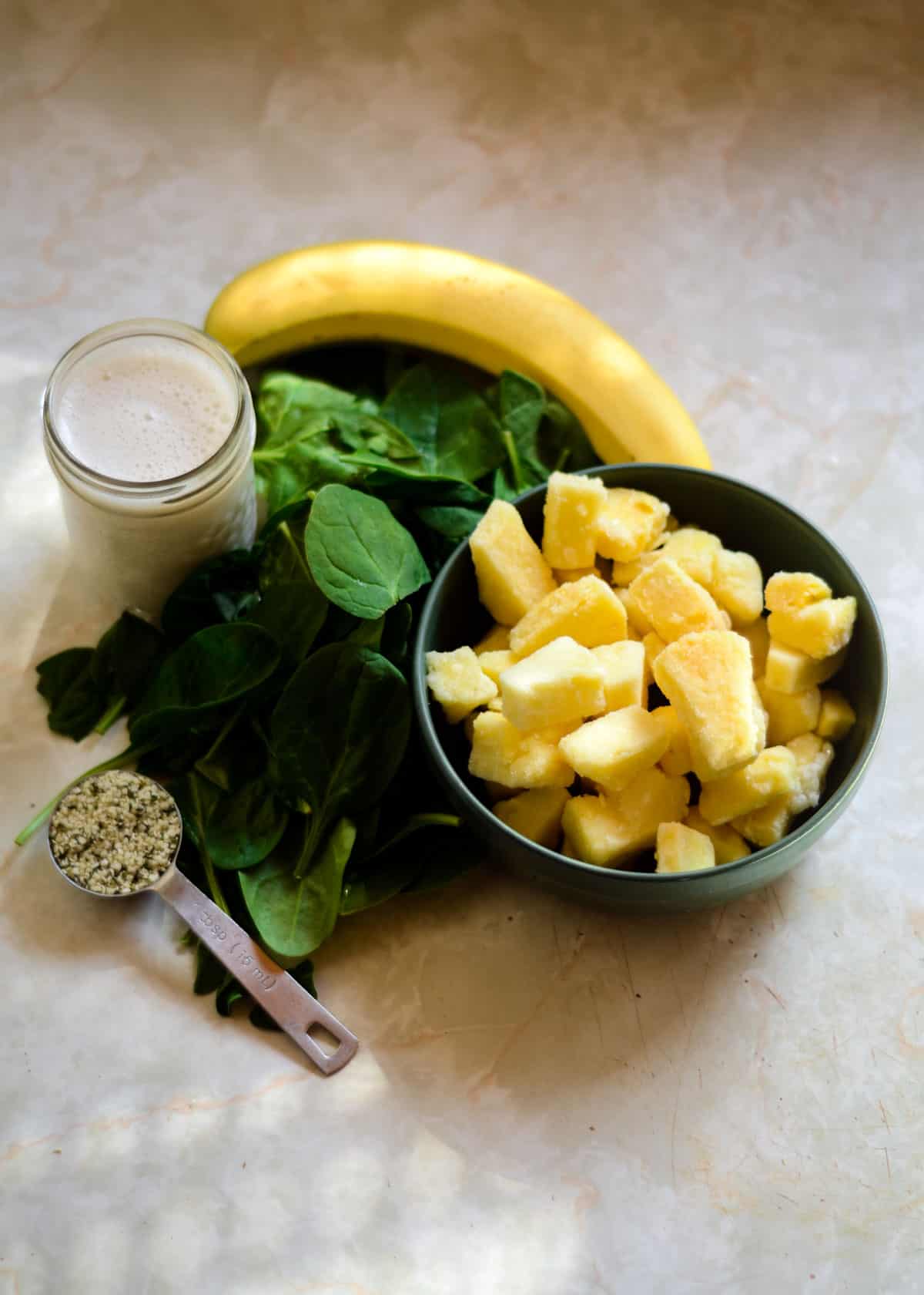 Spinach, frozen fruit - pineapple, banana, hemp hearts, milk on the counter for a smoothie.