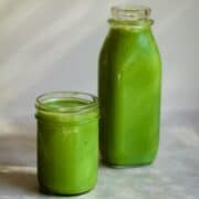 Bright green spinach smoothie in a small jar and a large juice bottle.