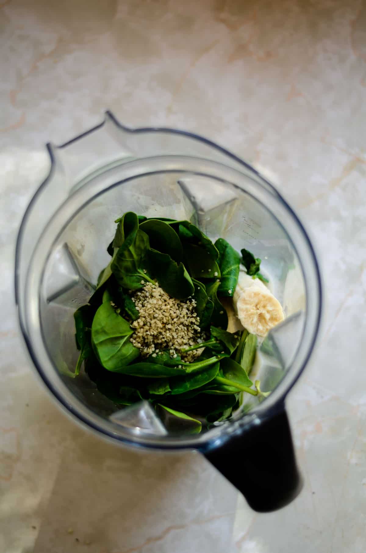 Banana, spinach, seeds, milk, in blender container for a smoothie.