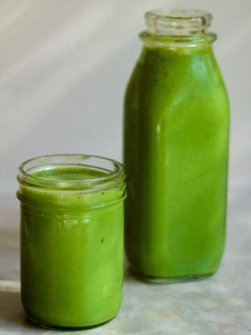 Bright green spinach smoothie in a small jar and a large juice bottle.