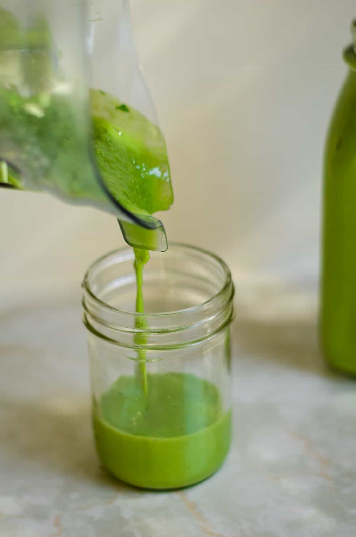 Pouring green smoothie from the vitamix blender into the smoothie cup.