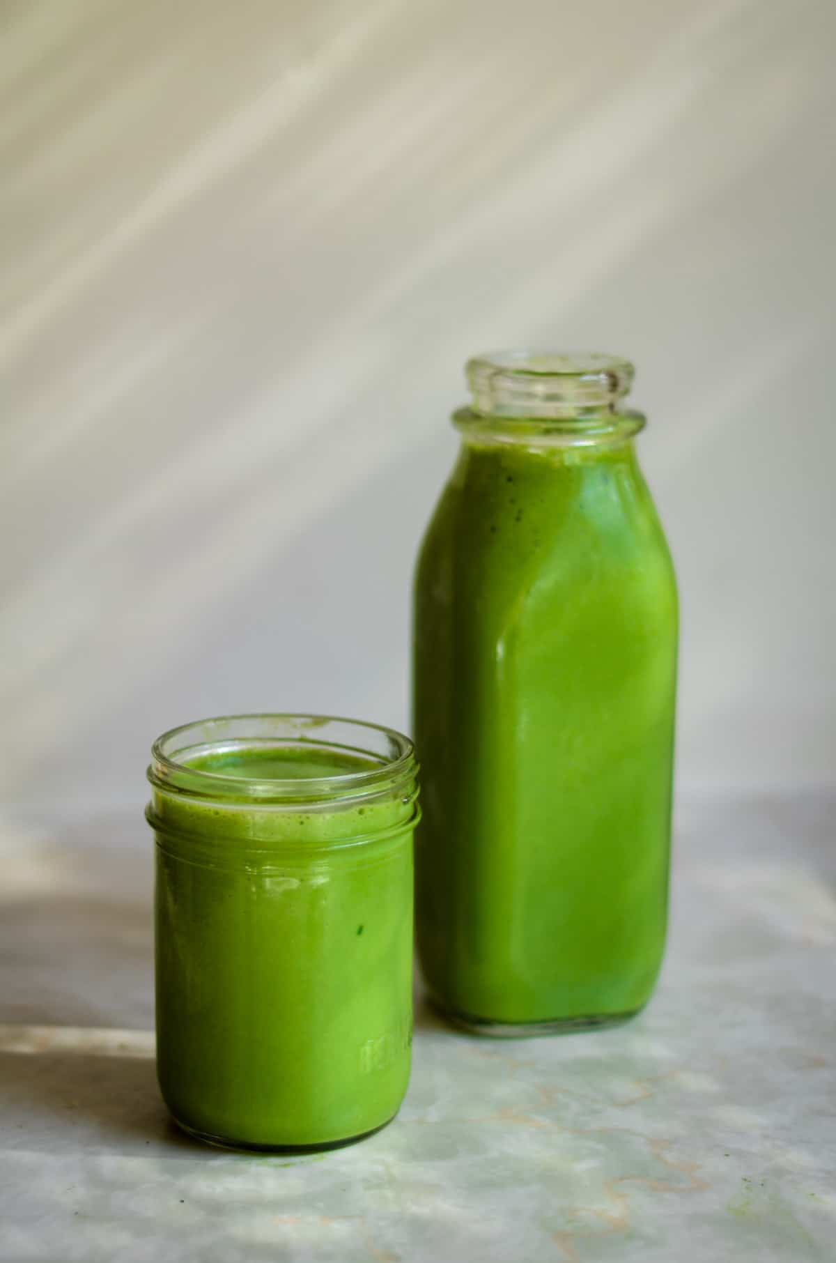 Two bright green spinach fruit smoothies, one in a small cup, the other in a juice bottle.