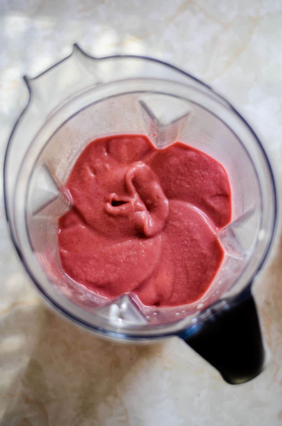 Thinner strawberry smoothie in blender container with more milk.
