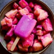 Dragon fruit popsicle with a bit gone in a bowl of frozen fruit.