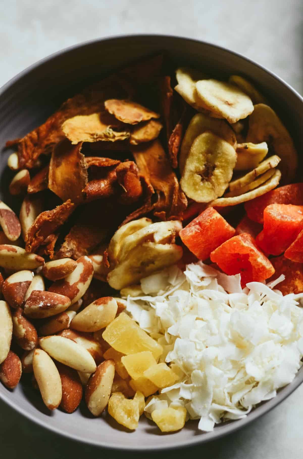 Bowl with dried bananas, dried papaya, dried mango, Brasil nuts, dried pineapples, dried coconut flakes.