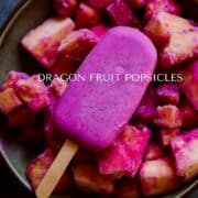 Bright purple popsicle sitting on top of frozen tropical fruit, pineapple, in a bowl.
