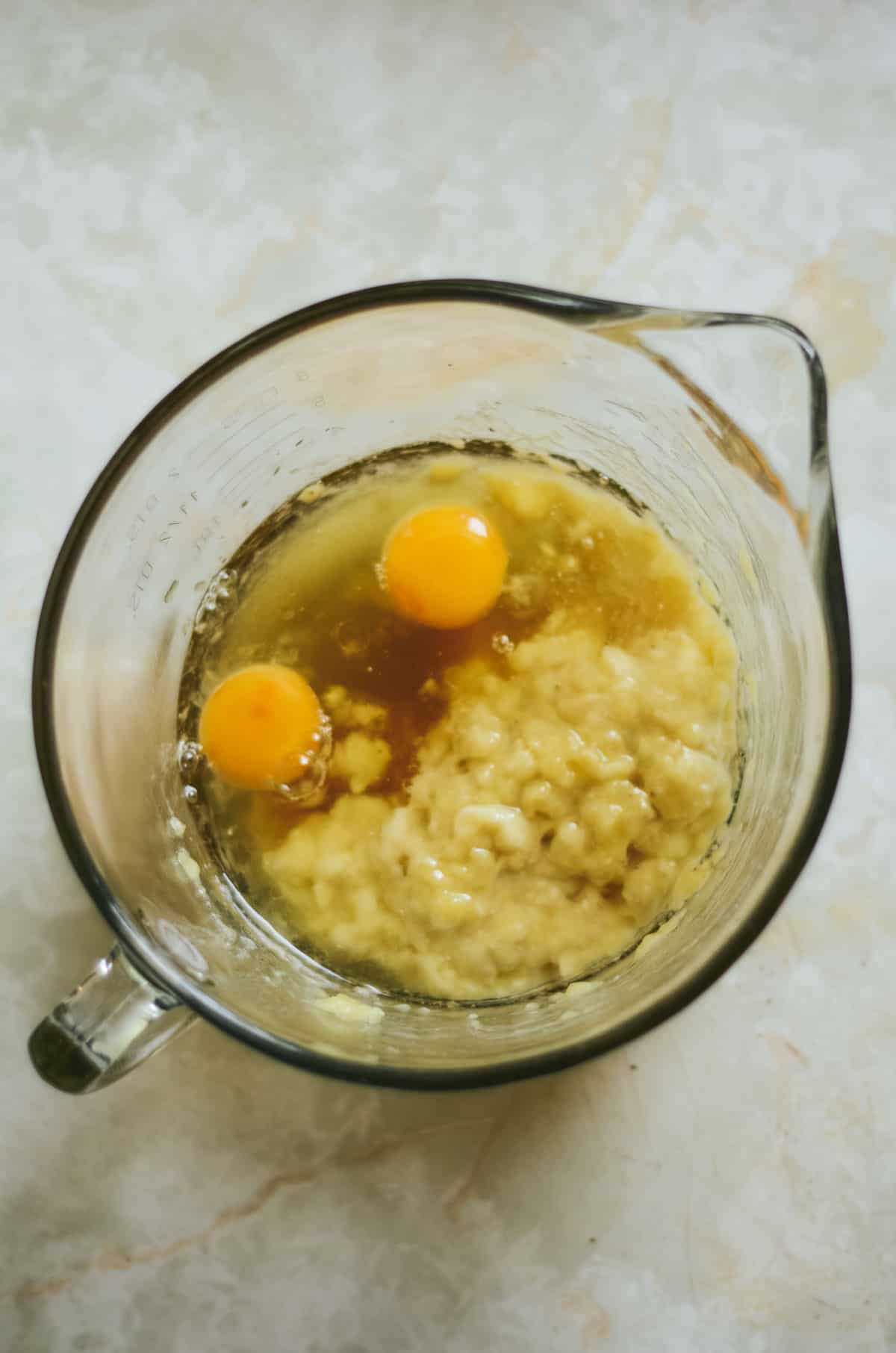 Eggs in a glass bowl with mashed banana for muffins.