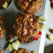 Brown muffin with pink rhubarb and brown sugar on top, sitting in a muffin tray.