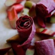 Pink fruit roll ups with rhubarb sitting around it.