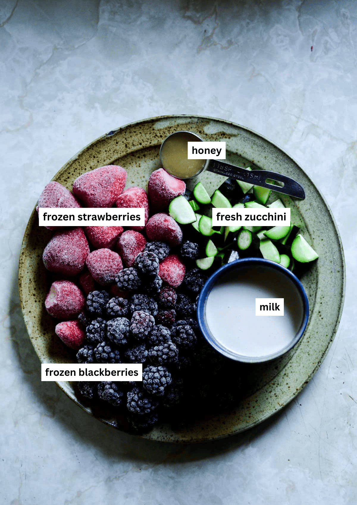 Frozen blackberries, frozen strawberries, cut zucchini, honey, and milk on a plate.