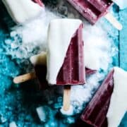 Homemade dark red sweet cherry popsicle yogurt dipped sitting on ice.
