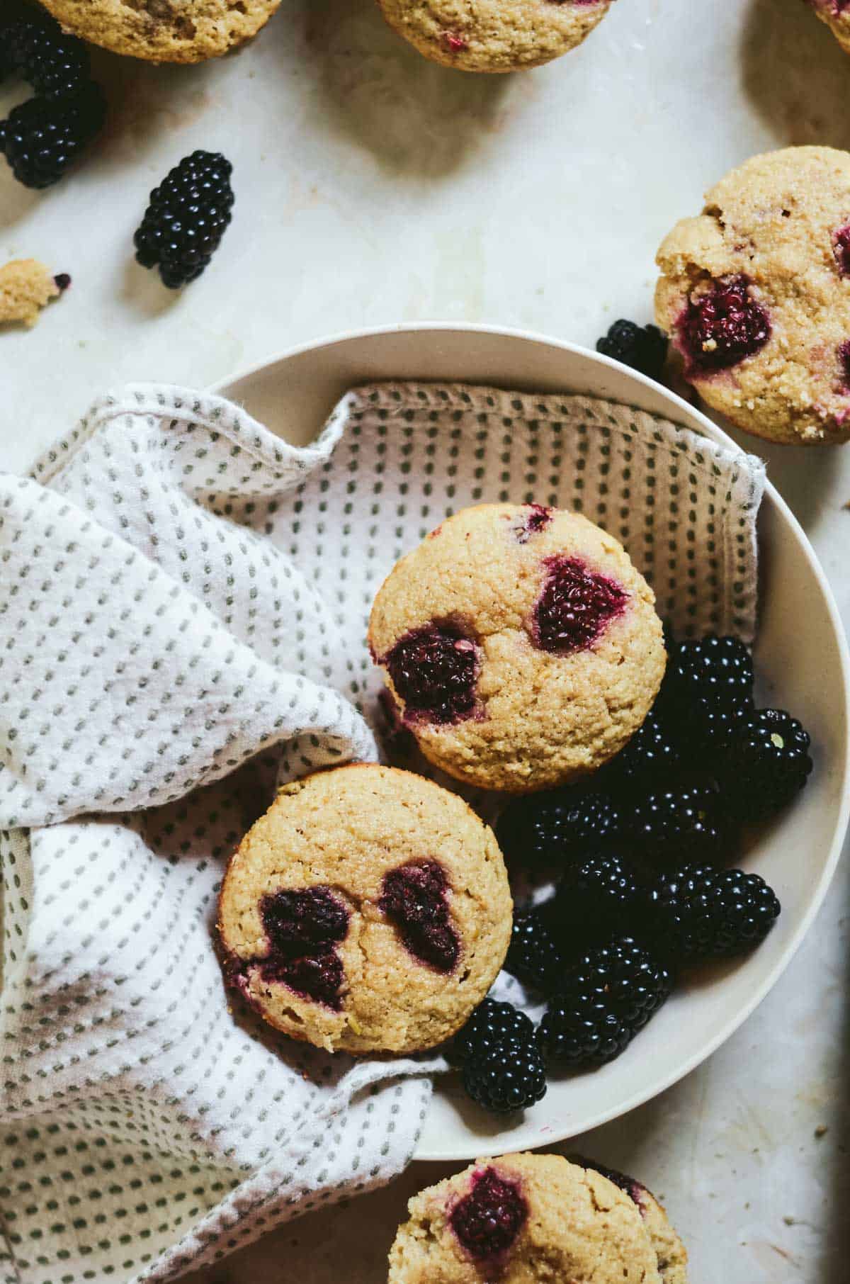 Blackberry muffins in a serving bowl with fresh blackberries in the bowl.