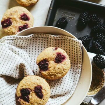 Fresh baked healthy gluten free blackberry muffins in a serving bowl, with fresh blackberries on the counter.