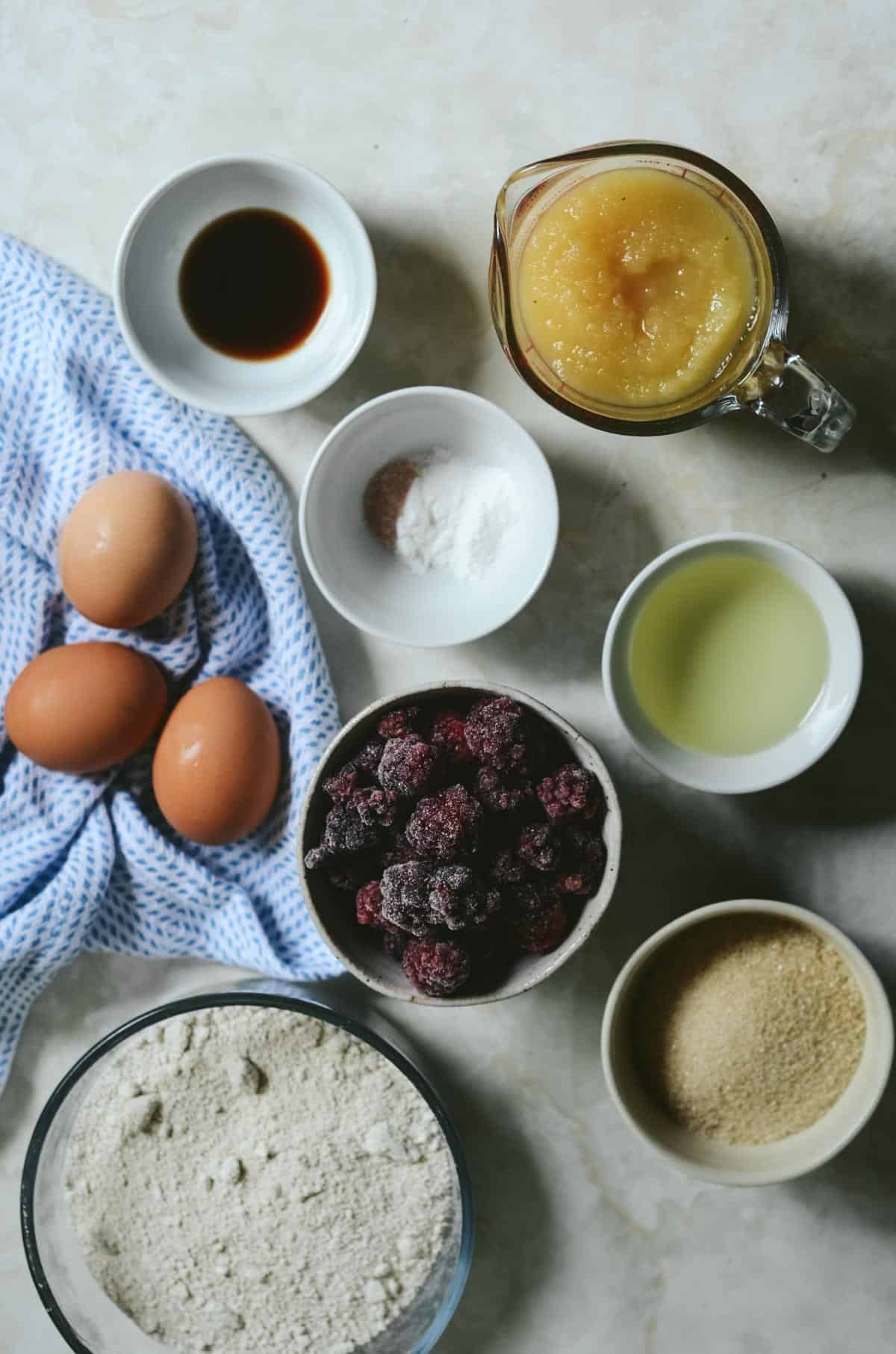 Eggs, vanilla, applesauce, oil, cane sugar, baking soda, sea salt, oat flour, frozen blackberries ready to make muffins.