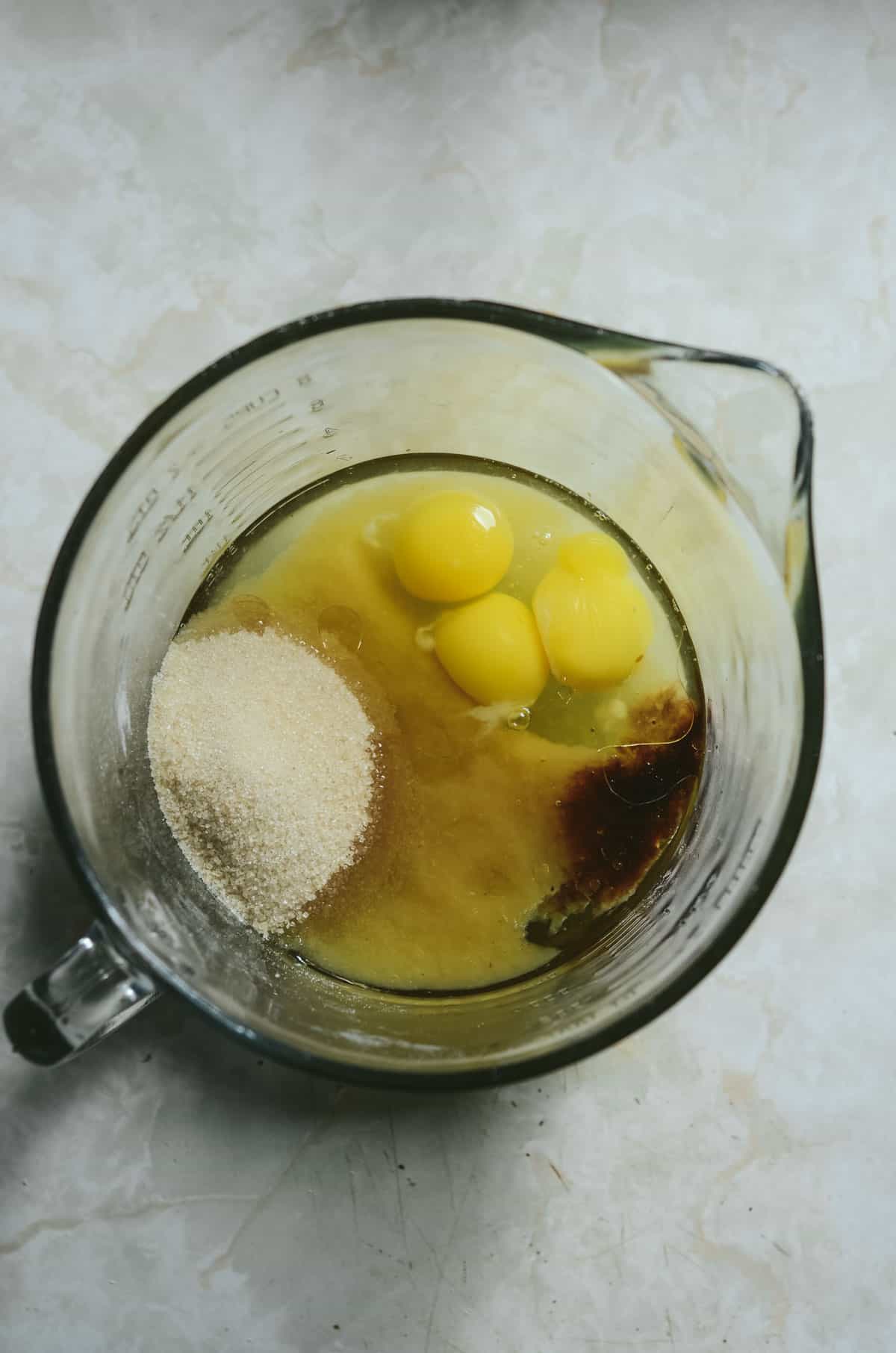 Mixing eggs, oil, vanilla, cane sugar, applesauce, in a glass bowl.